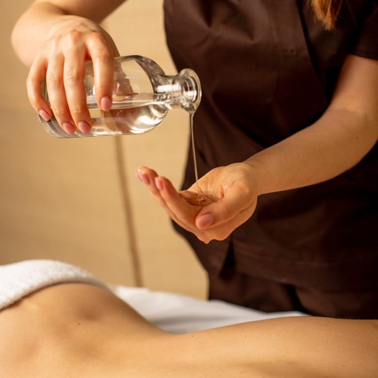 Closeup of masseur hands pouring aroma oil on woman back. Masseuse prepare to do relaxing treatment. Therapist doing oil massage on woman body.