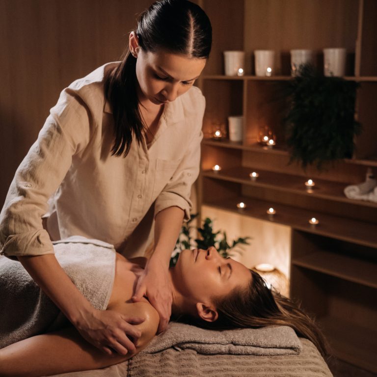A masseuse gives a body massage to a woman in a spa center. A professional masseur massages the shoulder of a girl lying in a spa center.